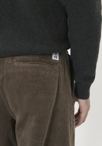 Bruine corduroy broek met een gestructureerd oppervlak en een achterzak. Een label met maat 'M' en nummer '73' is zichtbaar op de tailleband.