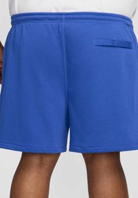 Blå bomullsshorts med enkel design, utrustade med elastisk midjeband, sidseams och en bakficka med klaff. Slät textur.