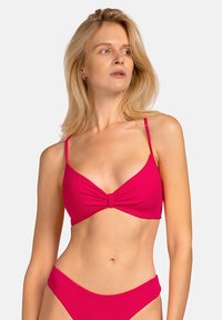Jasnoróżowy stanik bikini z zawiązanym węzłem na środku, cienkimi regulowanymi ramiączkami oraz gładką, elastyczną fakturą.