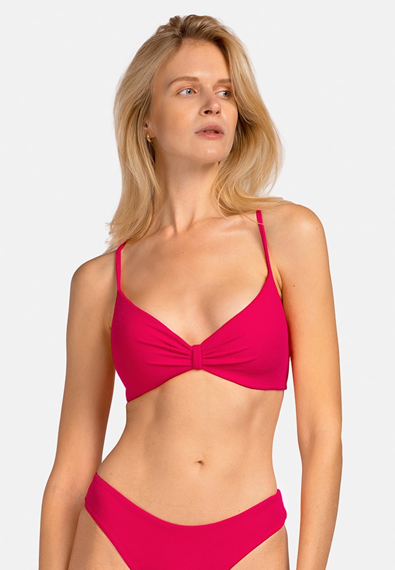 Jasnoróżowy stanik bikini z zawiązanym węzłem na środku, cienkimi regulowanymi ramiączkami oraz gładką, elastyczną fakturą.