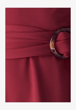 Tessuto di abito color bordeaux con una texture liscia, caratterizzato da un dettaglio in vita torcigliato e una grande fibbia in resina circolare.