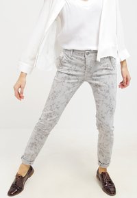 Ljust grå denimjeans med blommönster i dämpat rosa och grönt, slim fit och uppvikta muddar, i kombination med mörkbruna loafers.