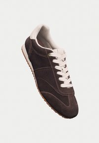 Sneaker in suede marrone con lacci bianchi, caratterizzato da una punta arrotondata, pannelli laterali testurizzati e una suola in gomma con un bordo marrone a contrasto.