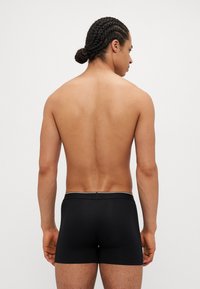 Schwarze Baumwoll-Boxershorts mit einem figurbetonten Design und einem kontrastierenden Bund. Der Rücken des Modells wird gezeigt, um die Shorts hervorzuheben.