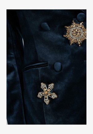 Blazer di velluto blu navy con spille floreali in oro e cristallo. Presenta un design doppiopetto e una texture liscia e raffinata.