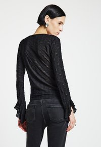 Schwarzes langärmliges Oberteil mit strukturierter Stoffqualität und ausgestellten Manschetten, kombiniert mit schwarzen Jeans mit Gesäßtaschen. Einfaches und elegantes Design.