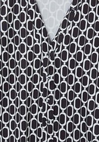 Black and white blouse featuring a geometric pattern of elongated ovals, with a V-neckline and button-down front. Smooth fabric texture.