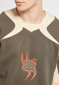 Felpa verde oliva con dettagli color crema, caratterizzata da una grafica arancione audace e stilizzata sul davanti e un design del collo unico.