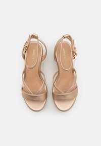 Strappy sandals in light metallic beige with a smooth finish, featuring a wide toe strap and thin cross straps. Silver hardware buckle detail.