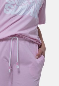 Rosa bomull t-shirt med texten "SUNDAIS" i vitt, turt med matchande rosa sweatpants som har en dragsko med vita och rosa ändar.