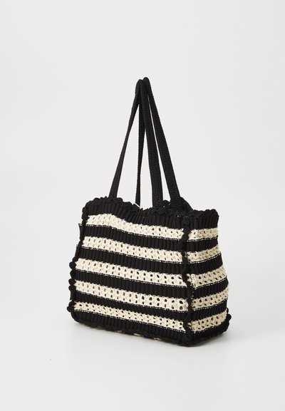 Torba tote w czarno-kremowe paski o plecionym wzorze, z mocnymi materiałowymi uchwytami i falistą górną krawędzią. Wyświetlony widok boczny.