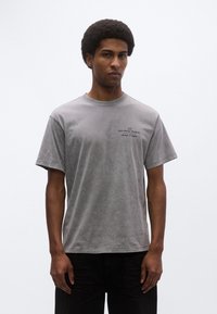 Γκρι βαμβακερό T-shirt με άνετη εφαρμογή, κοντά μανίκια και στρογγυλή λαιμόκοψη. Διαθέτει μικρό τυπωμένο λογότυπο στο στήθος.