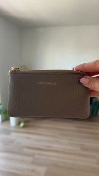 Brun lærpung med strukturert overflate, gullglidelås og logo preget på forsiden. Kompakt design, ideell for små nødvendigheter.