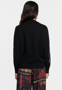 Maglione nero a maglia con collo rotondo e maniche lunghe, caratterizzato da intricate decorazioni floreali ricamate sulle maniche.
