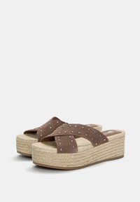 Sandali platform in suede marrone con cinturini incrociati decorati da borchie argentate, dotati di suola in iuta intrecciata e suola in gomma testurizzata.