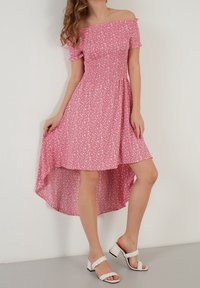 Vaaleanpunainen olkaimeton mekko, jossa on lyhyet uurrettu hihat, smockattu vartalo ja korkea-alareunus. Sisältää valkoisen kukkakuosin kauttaaltaan.