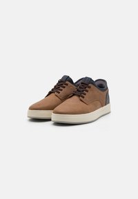 Brown leather sneakers with a smooth texture, white rubber sole, black accents, and round toe. Features lace-up design and padded collar.