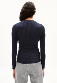Granatowa, prążkowana bluzka z długim rękawem o dopasowanym fasonie, okrągłym dekolcie i miękkiej fakturze. Połączona z jasnoszarymi dżinsami o wysokim stanie.