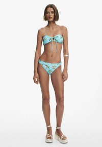 Bikini set s svetlomodrou tkaninou s kvetinovými vzormi. Vrchná časť je bez ramienok s predným viazaním a spodná časť má nízky strih.