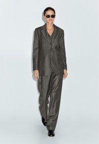 Grijs gestreept pak bestaande uit een op maat gemaakte blazer en losse broeken, gecombineerd met zwart zonnebrillen en slanke zwarte schoenen.