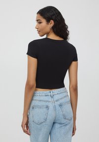 Czarna krótka koszulka z krótkim rękawem, okrągłym dekoltem i gładką fakturą, w połączeniu z jasnoniebieskimi dżinsami z tylnymi kieszeniami.