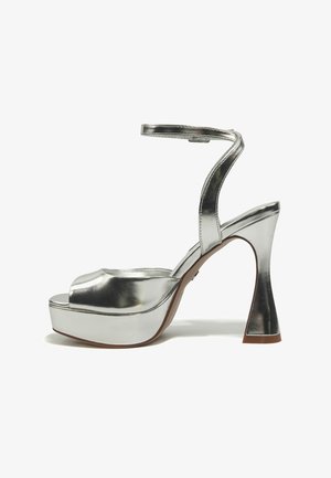 Sidabrinės aukštakulnės basutės su platformos padu ir čiurnos dirželiu, išlenktu bloko kulnu, atviru priekeliu ir metaliniu blizgesiu.