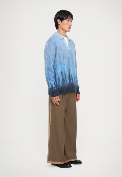 Maglione a maglia blu con gradienti, a maniche lunghe, con colletto e vestibilità ampia, abbinato a pantaloni larghi marroni e scarpe nere.