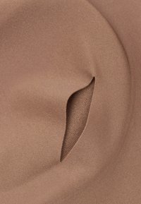 Close-up van een bruine stof met een kleine opening die een gestructureerde brei eronder toont.