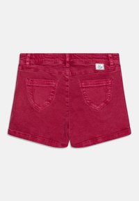 Pantalones cortos de mezclilla rojos con una textura suave, dos bolsillos traseros y una etiqueta cosida. Presenta una cinturilla estándar y un corte recto.