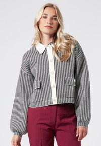 Rutigt svart och vitt kort jacka med vit krage, oversized ärmar, knäppning framtill och fickor. Lämplig för avslappnad användning.