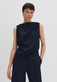 Navy sleeveless top with a relaxed fit, smooth texture, round neckline, and subtle draping. Paired with matching tailored trousers.