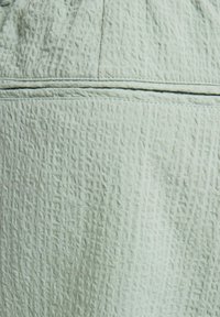 Light green textured fabric featuring a crinkled surface with subtle patterns and a seam running horizontally across the middle.