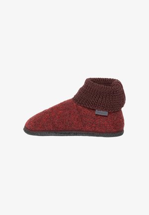 Roter Wollhausschuh mit dunkelbraun gestricktem Bündchen und schwarzer Sohle, Seitenansicht, mit kleinem Stoffmarkenetikett am Bündchen.