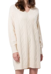 Cremefarbenes Strickkleid mit V-Ausschnitt, langen Ärmeln und strukturierten Rautenmuster. Hergestellt aus weichem, leichtem Stoff.