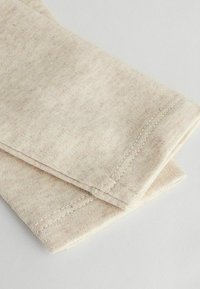 Ljust beige tyg med en mjuk textur, med stickade sömmar och en vikt kant. Materialet har subtila fläckar av färg.
