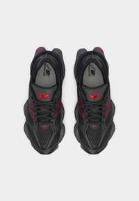 Ζευγάρι μαύρα και κόκκινα παπούτσια για τρέξιμο New Balance με χοντρές σόλες, φωτογραφημένα από πάνω σε λευκό φόντο.