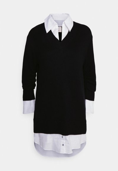 Schwarzer Strickpullover mit V-Ausschnitt, über ein weißes Hemd mit Kragen getragen. Der Pullover hat lange Ärmel mit weißen Besatz an den Bündchen.