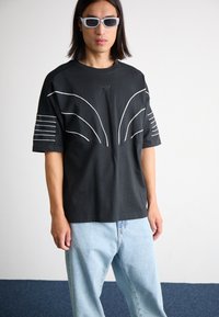 Black short-sleeve T-shirt with white line patterns on the front and striped accents on the sleeves. Paired with light blue jeans.