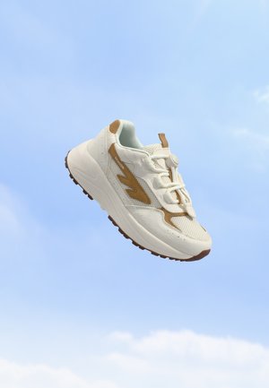 Baskets blanches et marron avec une semelle épaisse et des lacets élastiques à bouton-pression sur un fond de ciel bleu clair.