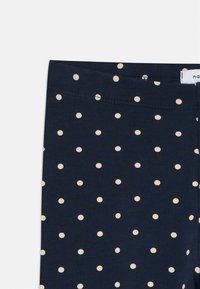 Sötétkék leggings puha pamutból, fehér pöttyökkel. Simított derékpánttal rendelkezik, amelyen egyenletesen elosztott, kicsi pöttyös minta található.