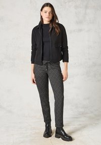 Giacca nera con zip e tasche laterali, abbinata a pantaloni neri e bianchi con un motivo a diamante, e stivaletti neri alla caviglia.