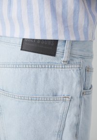Light blue denim jeans with a textured surface, featuring a black leather patch labeled "ONLY & SONS" on the back pocket.