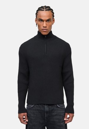 Maglione nero a costine con colletto alto e chiusura con zip a un quarto. Realizzato in materiale a maglia testurizzato, presenta maniche lunghe e un design aderente.
