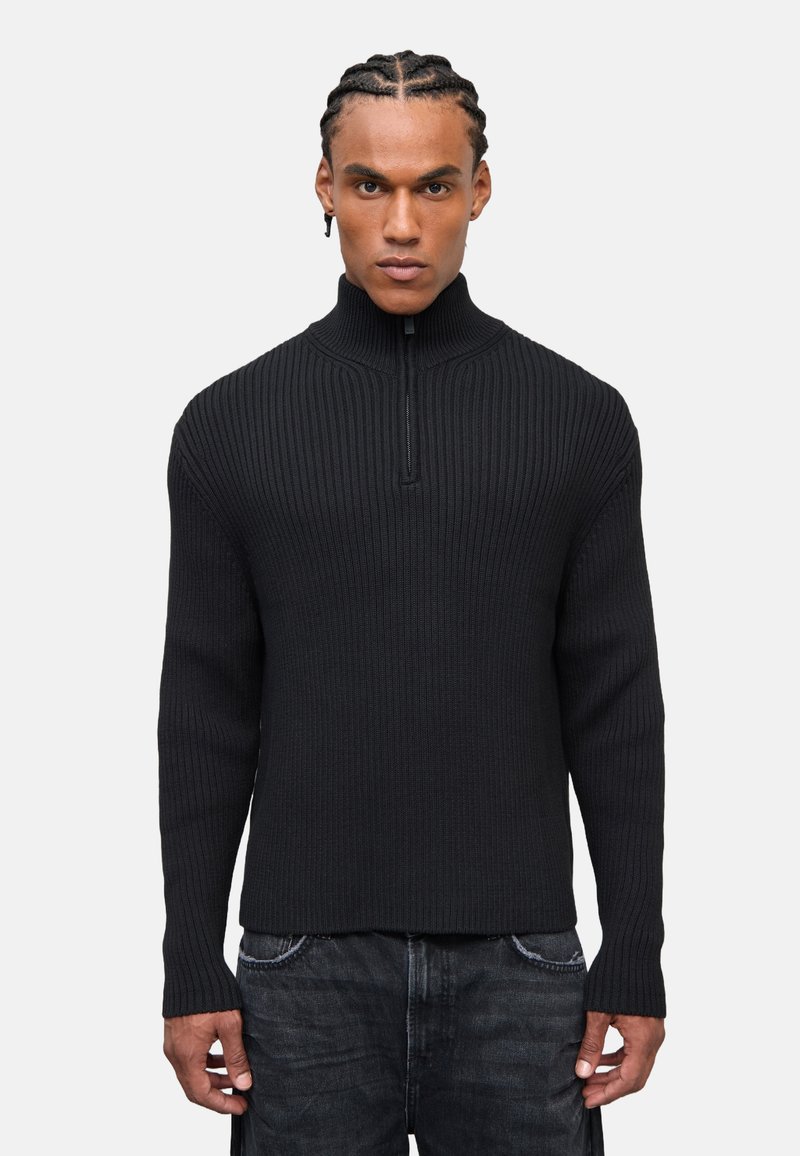 Schwarzer gerippten Pullover mit hohem Kragen und Viertelreißverschluss. Hergestellt aus strukturiertem Strickmaterial, mit langen Ärmeln und tailliertem Design.