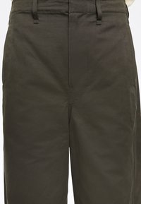 Pantaloni verde scuro realizzati in tessuto testurizzato con cuciture visibili, vita piatta e tasche laterali; design a gamba dritta.
