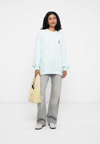 Šviesiai mėlynas ilgomis rankovėmis džemperis, derinamas su pilkais plačiais kelnėmis. Laikoma šviesiai geltona rankinė. Baltos batai su juodais padais.