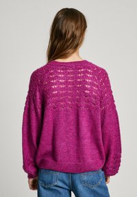 Magenta megzta palaidinė laisvu kirpimu, su tekstūruota nėrinių apykakle ir guma prie rankovių. Minkšta medžiaga su jaukia išvaizda.