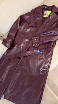 Burgunderfarget faux skinn trenchcoat med en glossy, teksturert overflate, brede revers, belte i livet og to sidelommer.