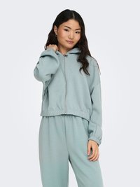 Lichtgroene cropped zip-up hoodie met capuchon en elastische boorden, gecombineerd met bijpassende joggingbroek. Zachte stof en een losse pasvorm.