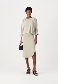 Lys beige, flytande topp med bred u-ringning och skärmsläpp ärmar, i kombination med en knälång, figurnära kjol. Svarta klacksandaler med blockklack och en liten väska.